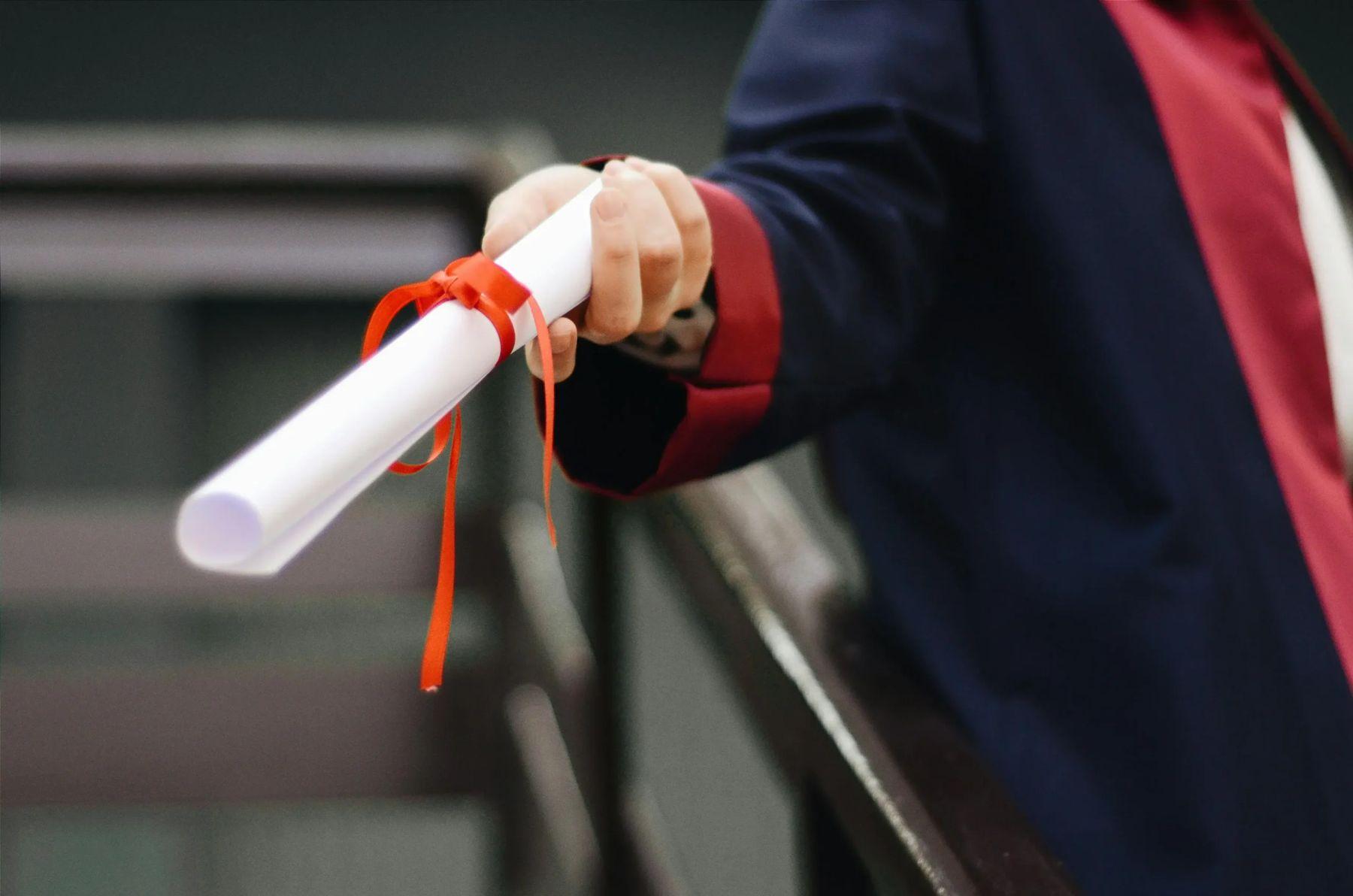 Graduate holding a rolled diploma tied with a red ribbon